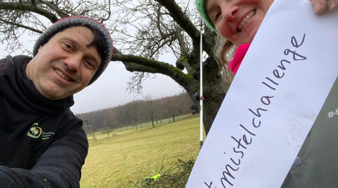 Zwei Personen halten ein Schild hoch mit #mistelchallenge